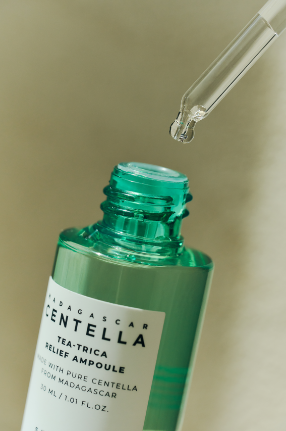 YABUKO SKIN1004 Madagascar Centella Tea-Trica nomierinoša ampula ar zaļām lapām un pudeli uz balta fona